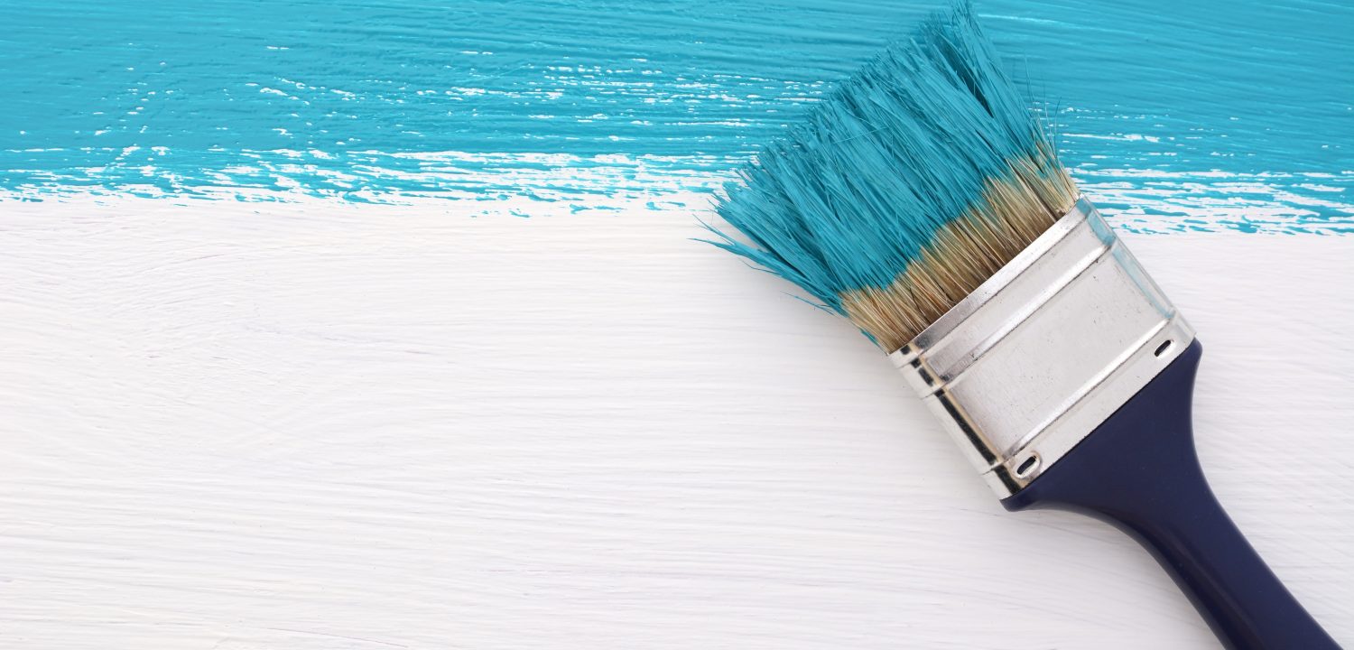 Horizontal stripe of turquoise paint with a dirty paintbrush on a white wooden board